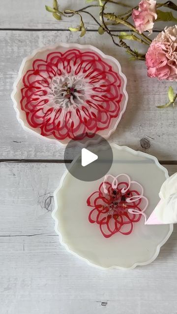 two plates with red and white designs on them sitting next to pink flowers in vases