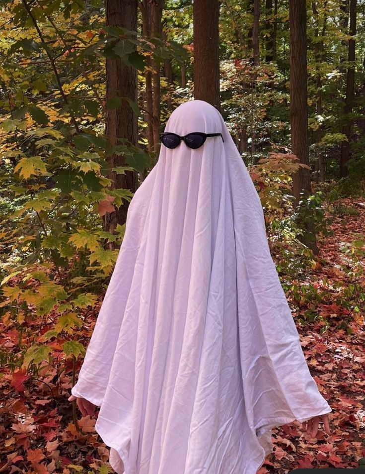 a person in a white ghost costume with sunglasses on their head standing in the woods