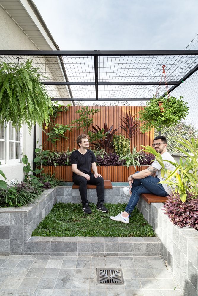 two men sitting on benches in the middle of a yard with plants and greenery