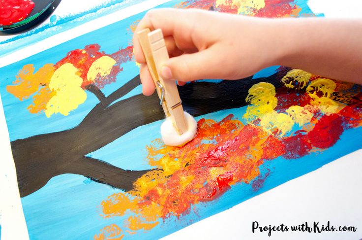 a child's hand holding a paintbrush over an art project with trees painted on it