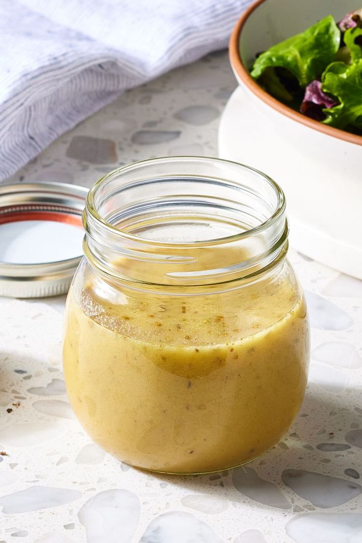 a glass jar filled with mustard next to a bowl of lettuce and a spoon