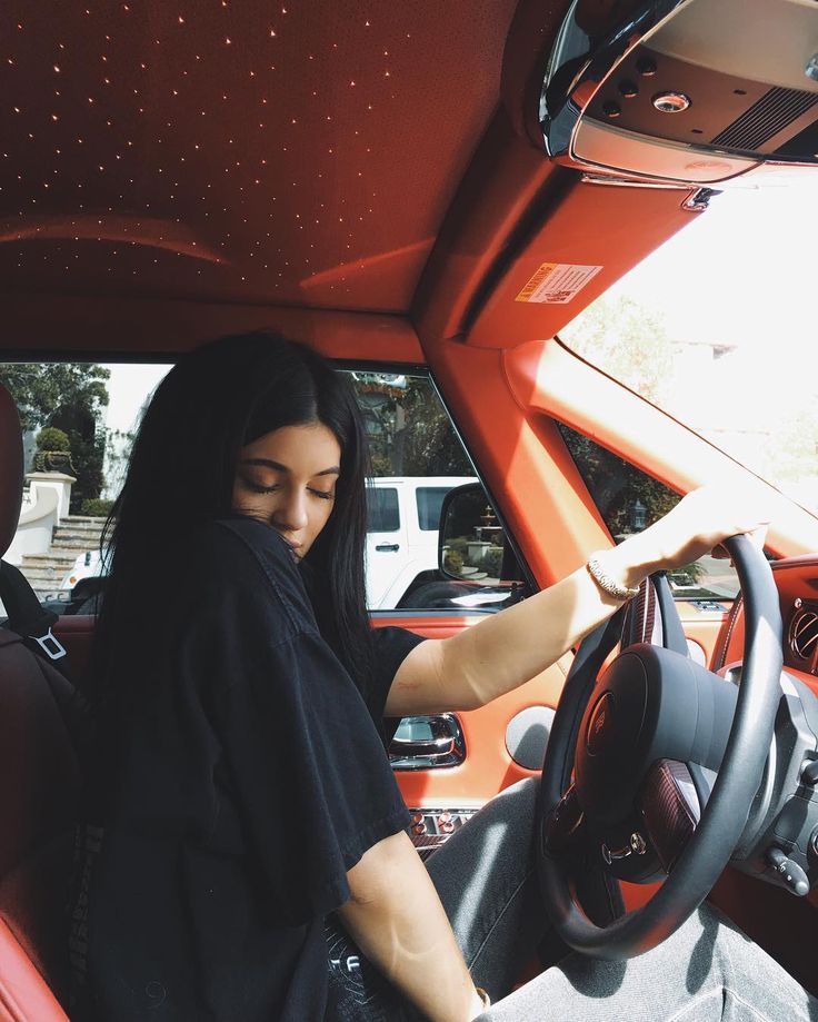 a woman sitting in the driver's seat of a red car with her hands on the steering wheel