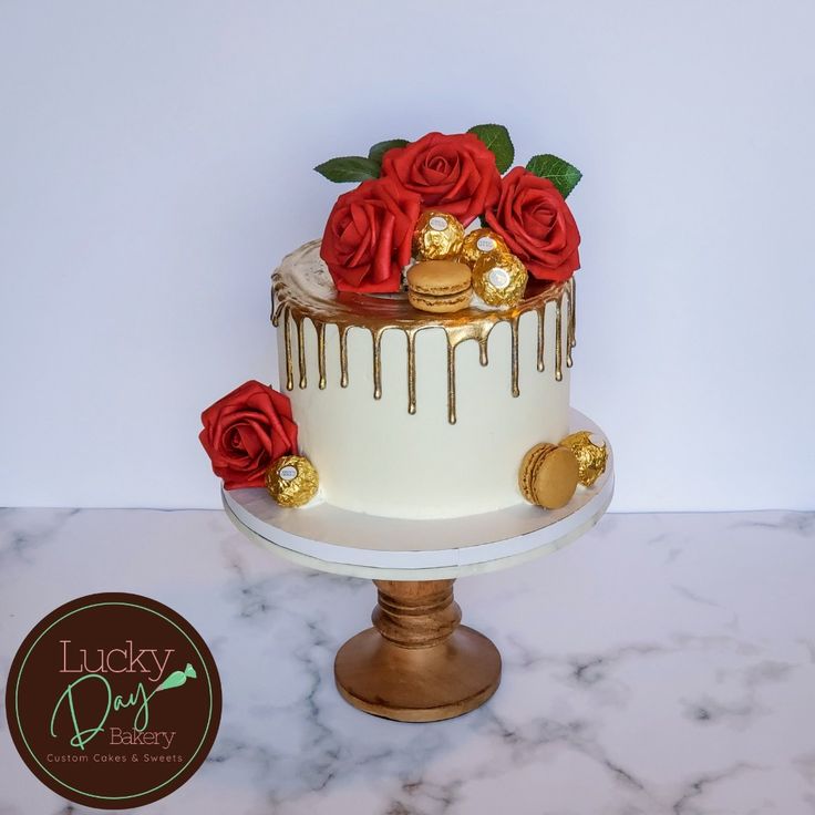 a white and gold cake with red roses on top, sitting on a marble table