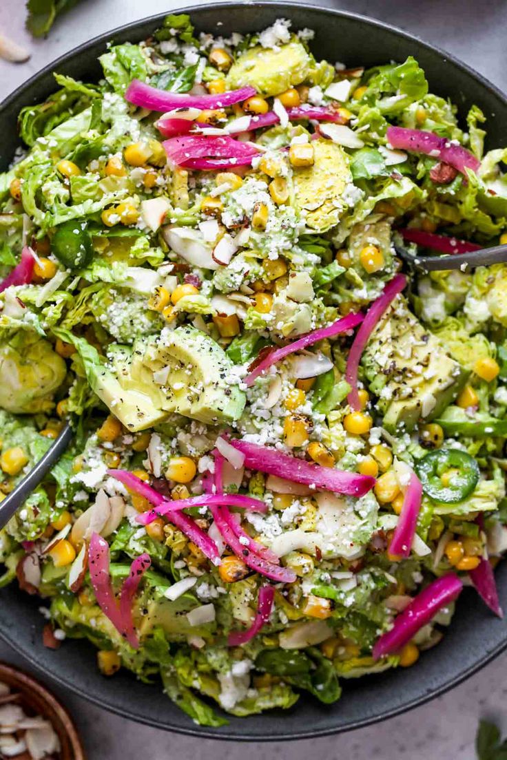 a salad with red onions, corn and dressing in a black bowl on a table