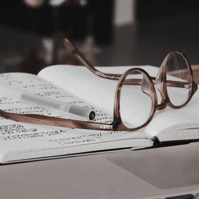 a pair of glasses resting on an open book next to a pen and eyeglasses