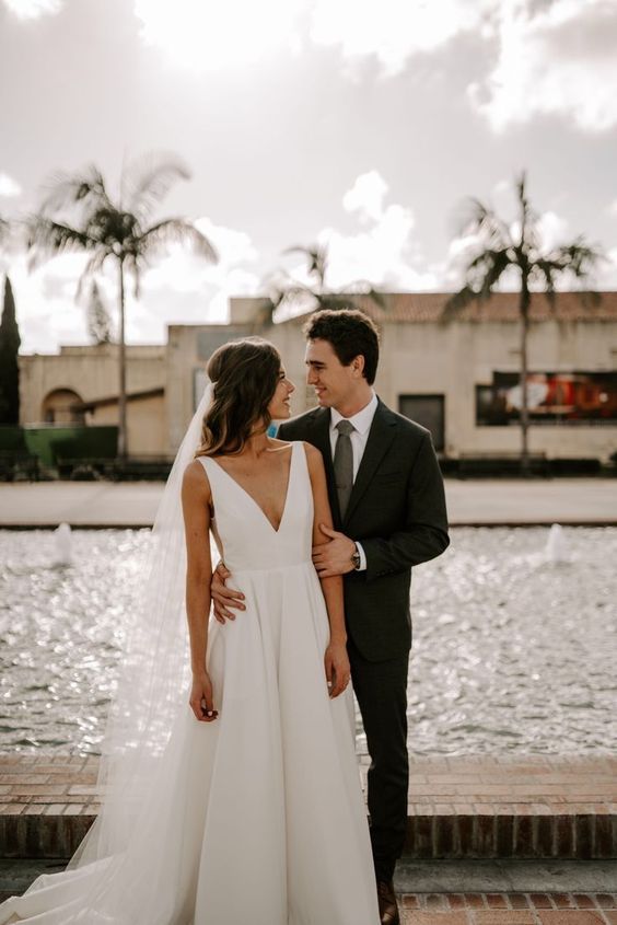 a bride and groom standing next to each other in front of a fountain with palm trees