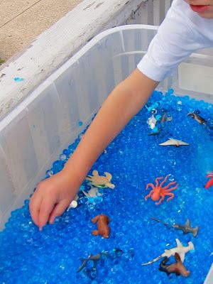 a young boy playing with toys in a plastic container filled with blue water and sand