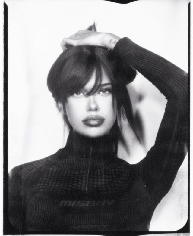 a black and white photo of a woman with her hands on her head, wearing a turtle neck sweater