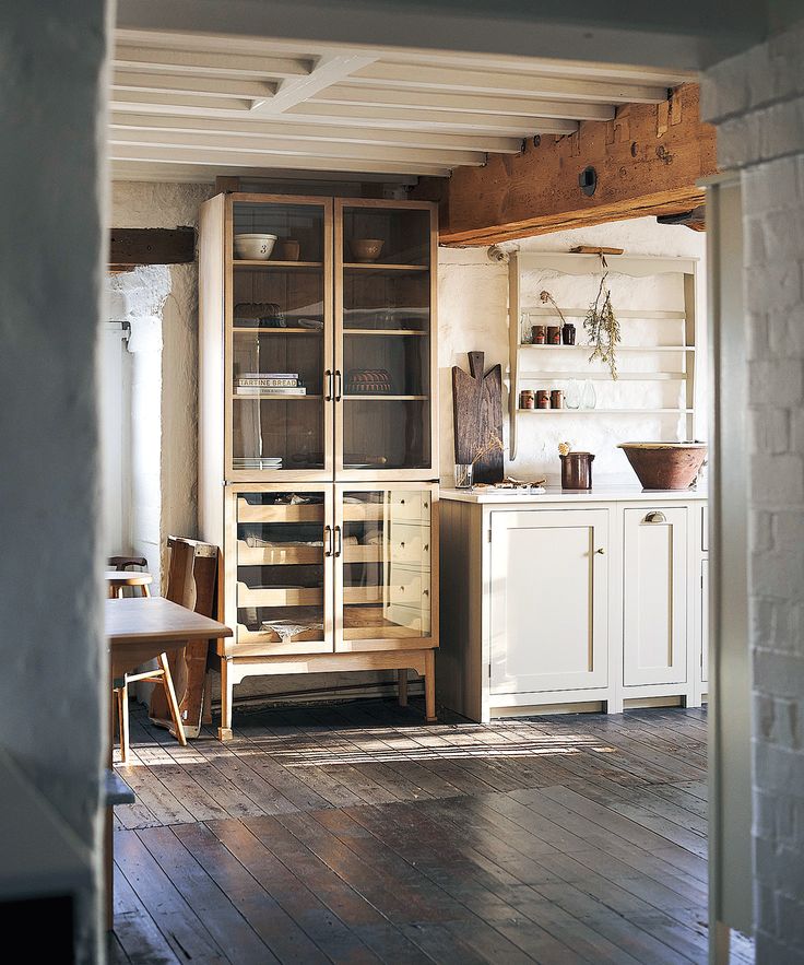 an old fashioned kitchen with wooden floors and white cupboards in the middle of it