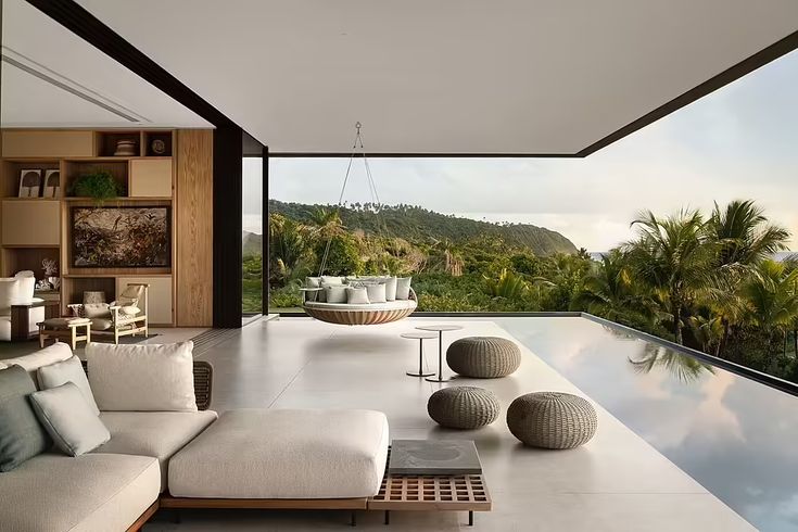 a living room filled with furniture next to a large window covered in plants and trees