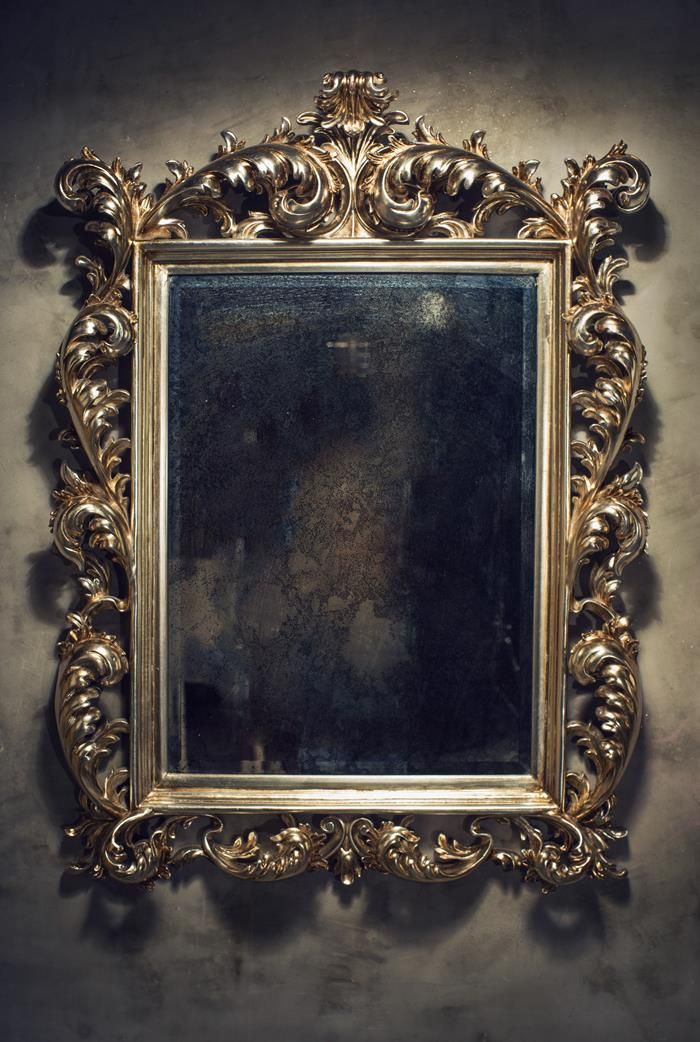 an ornate gold framed mirror hanging on the side of a wall in a dark room