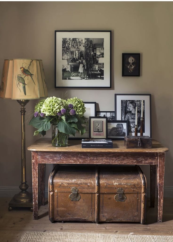 a wooden table with flowers and pictures on it next to a lamp in a living room