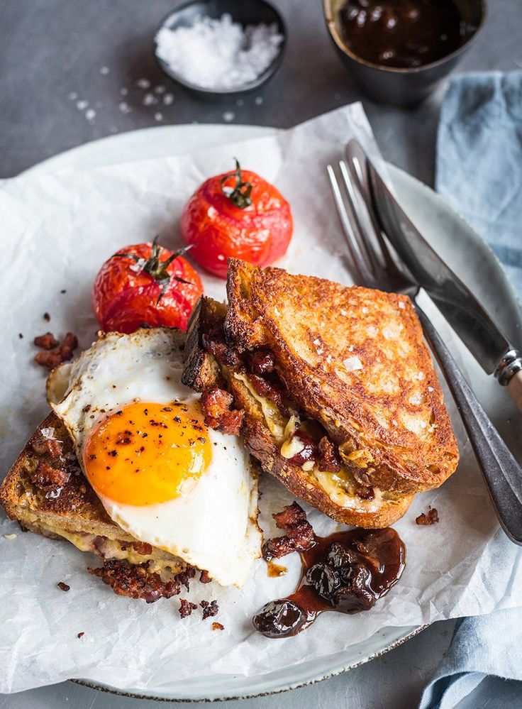 an egg and toast sandwich with tomatoes on the side