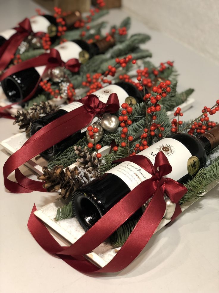 three bottles of wine are wrapped in red ribbon and decorated with pine cones, berries, and holly