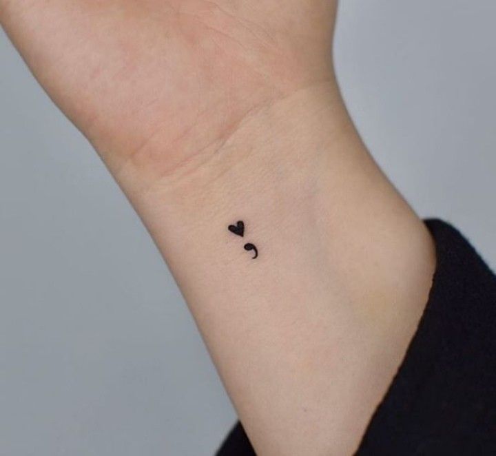 a small black heart tattoo on the wrist