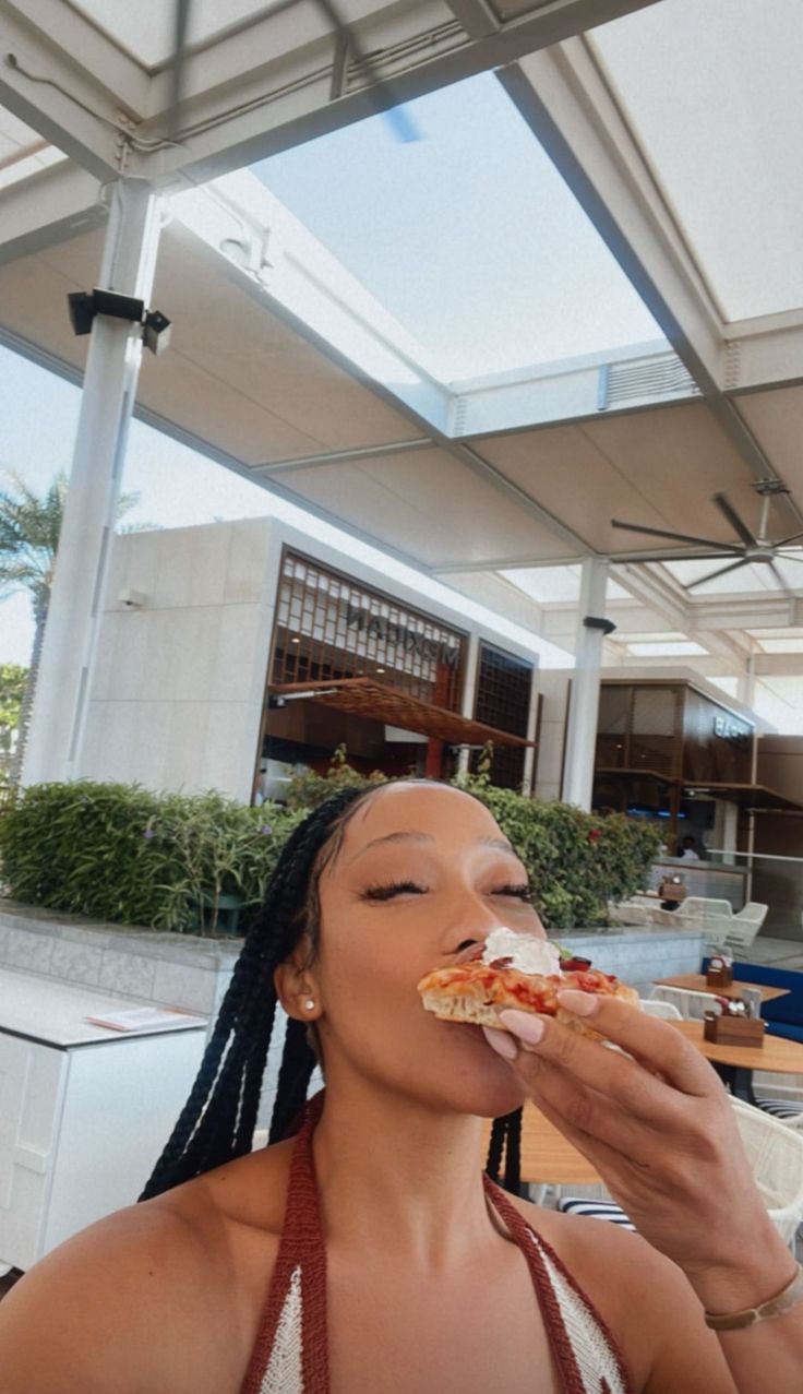 a woman eating a slice of pizza on top of a table in front of an outdoor dining area