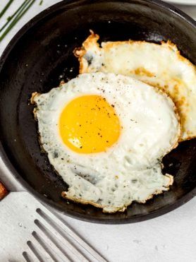 two fried eggs in a frying pan on top of a table with silverware