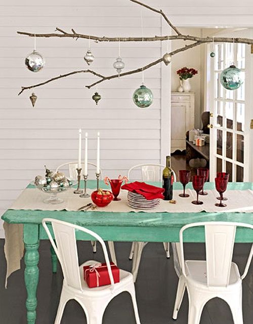 a dining room table with white chairs and christmas ornaments hanging from the branches above it