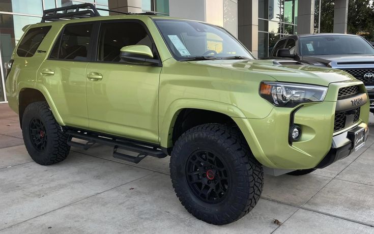 a lime green toyota 4runner is parked in front of a building with two other vehicles