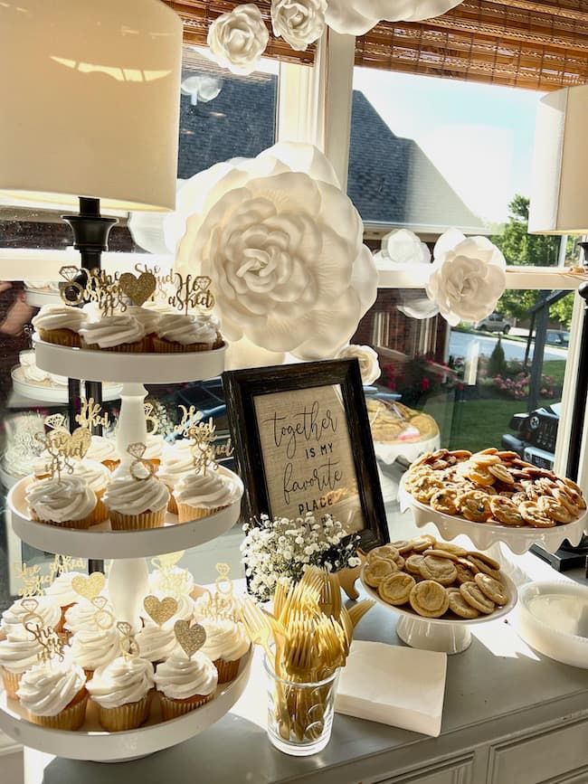 a table topped with lots of cupcakes and pastries next to a window