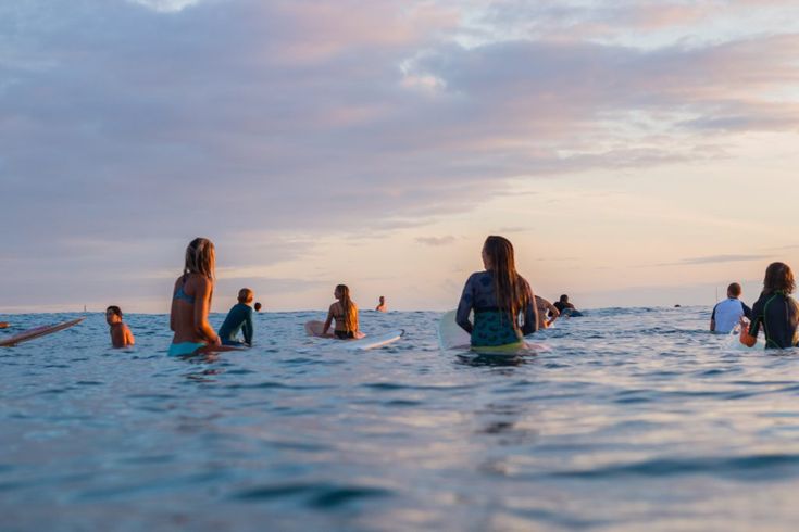 a group of people sitting on surfboards in the ocean at sunset or sunrise time