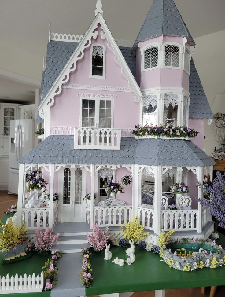 a pink and white doll house with flowers in the front yard