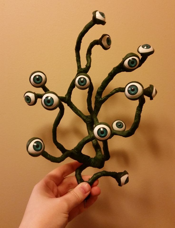 a hand holding up a fake tree with eyes on it's leaves and branches