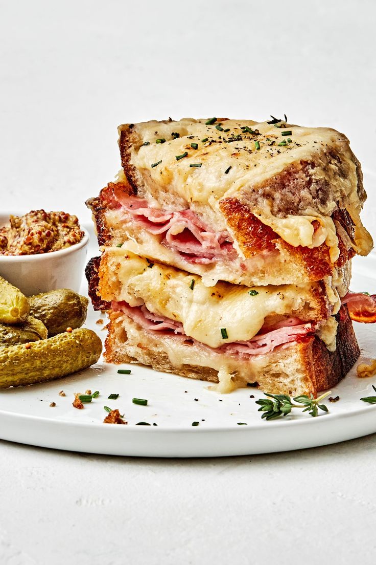 a white plate topped with a cut in half sandwich next to a bowl of pickles