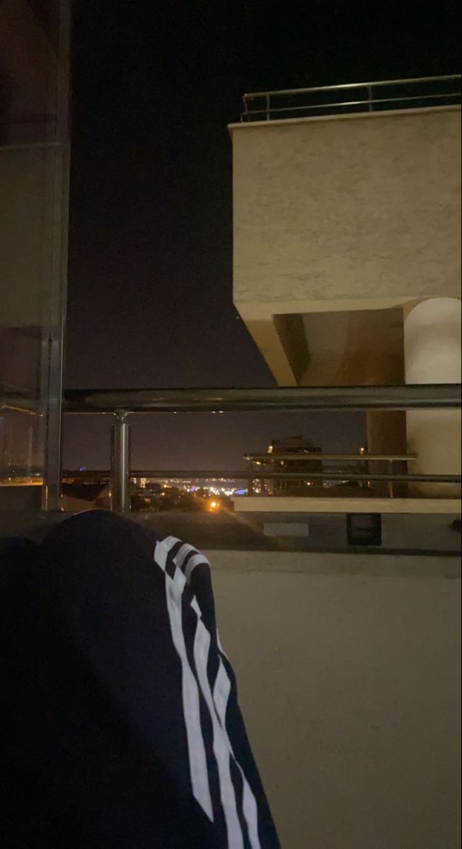 a man sitting on top of a roof next to a tall building at night with the city lights in the background