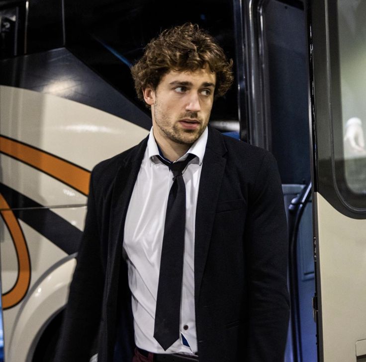 a man wearing a suit and tie standing in front of a bus with his hands in his pockets