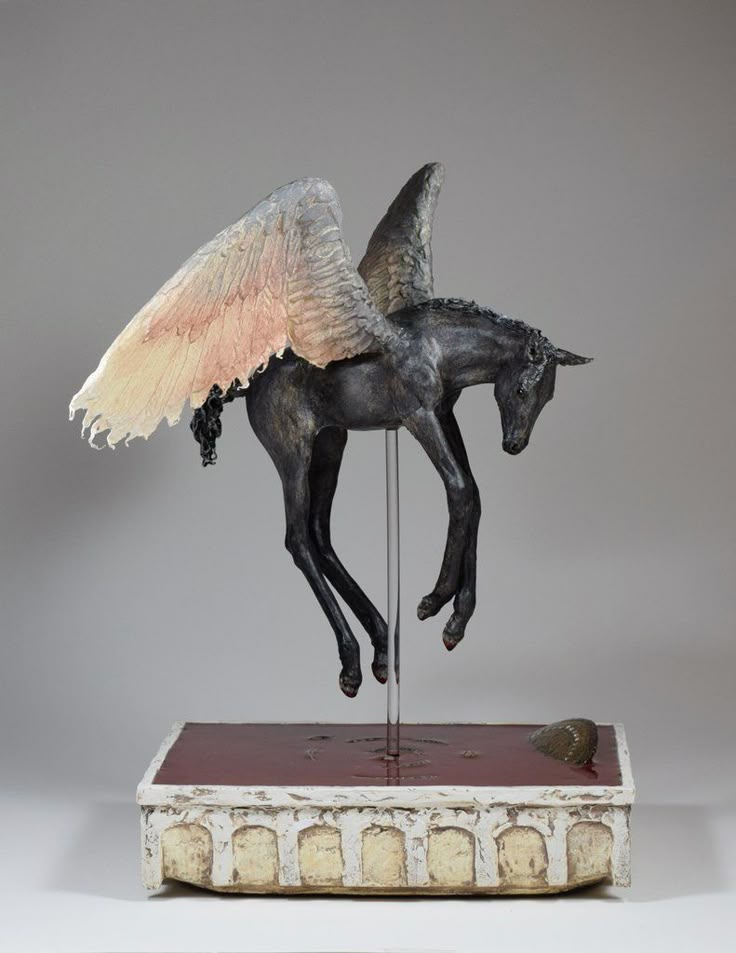 a statue of a horse with wings on it's head and tail, standing on a book