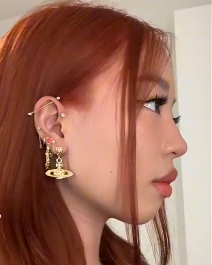 a close up of a person with red hair wearing ear rings and earrings on their ears