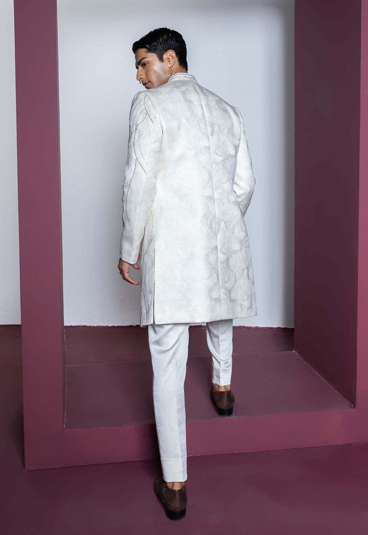 Embrace sophistication with a dull gold embroidered Jacquard jacket paired with a front-open kurta featuring fine pleating details on the placket. Complete the ensemble with matching pants, achieving a harmonious blend of opulence and intricate design for a refined and stylish look. Elegant Semi-formal Sets For Eid, Nehru Jacket With Naqshi For Reception, Straight Kurta, Nehru Jacket With Naqshi For Reception, Elegant Straight Kurta With Set-in Sleeves, Classic Bandhgala For Eid Festivities, Classic Bandhgala For Eid Festival, Elegant Formal Outerwear With Chikankari Embroidery, Formal Chikankari Embroidery Straight Kurta Bandhgala, Designer White Raw Silk Bandhgala