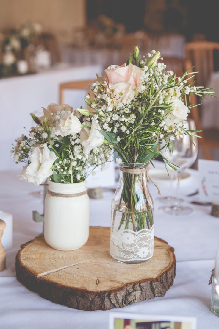 two vases filled with flowers sitting on top of a wooden slice at a table