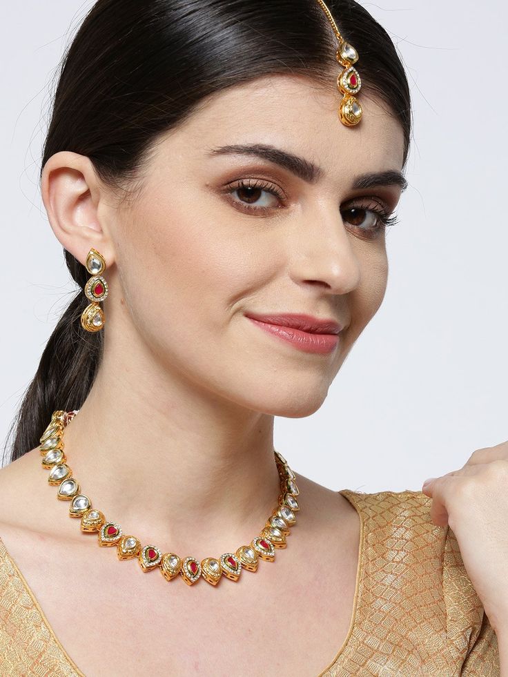 This handcrafted jewelry set consists of a necklace, a maang tikka and a pair of matching drop earrings. The necklace has a maroon color-theme with green accents, comes with kundan stone studs, is gold-plated, and secured with an adjustable drawstring closure. A matching maang tikka comes with kundan stone studs, is gold-plated, and can be secured with a hook closure. A pair of matching drop earrings come with kundan stone studs, are gold-plated, and are secured with a post and back closure. The Festive Dual-tone Gold Plated Jewelry, Dual-tone Chandbali Jewelry For Puja, Dual-tone Kundan Jewelry, Festive Dual-tone Temple Jewelry Sets, Dual-tone Gold Plated Jewelry, Kundan Necklaces With Latkans For Diwali, Gold Plated Kundan Necklace With Latkans For Gift, Kundan Jewelry With Stone Work For Navratri, Chandbali Jewelry Sets For Puja