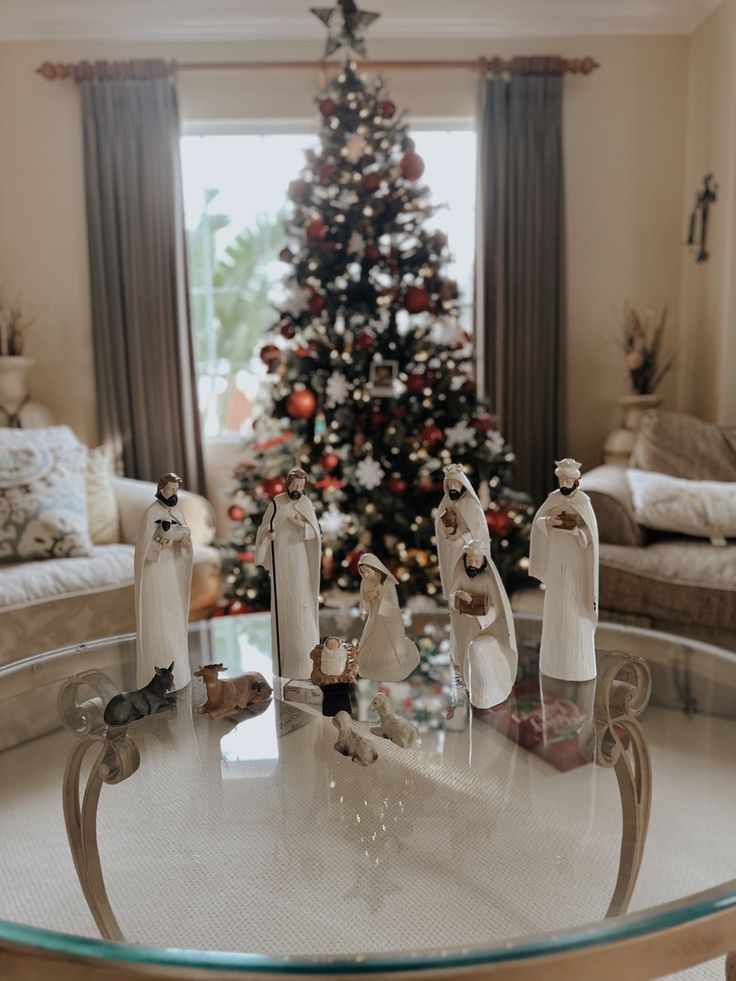 a living room with a christmas tree in the corner and two figurines sitting on a glass table