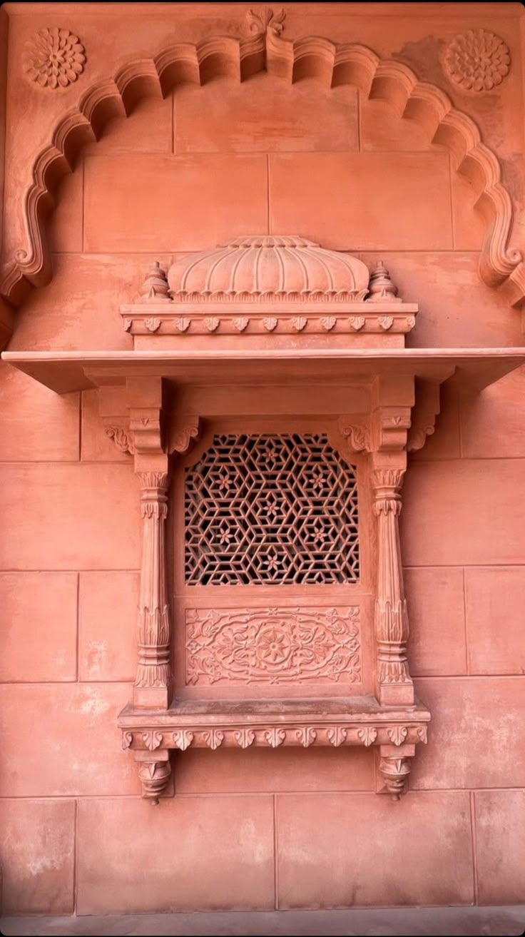 an intricately carved window on the side of a pink building with carvings and arches