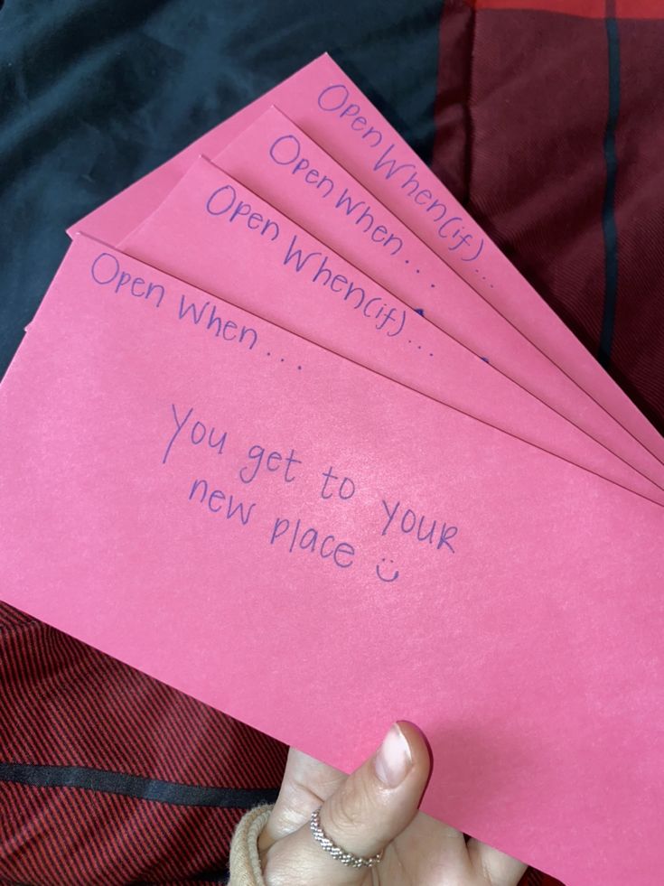 four pink envelopes with writing on them are held up by a woman's hand