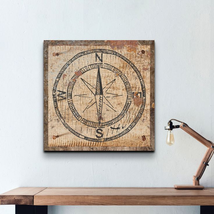 a wooden table with a lamp on it and a wall hanging above it that has an old compass design