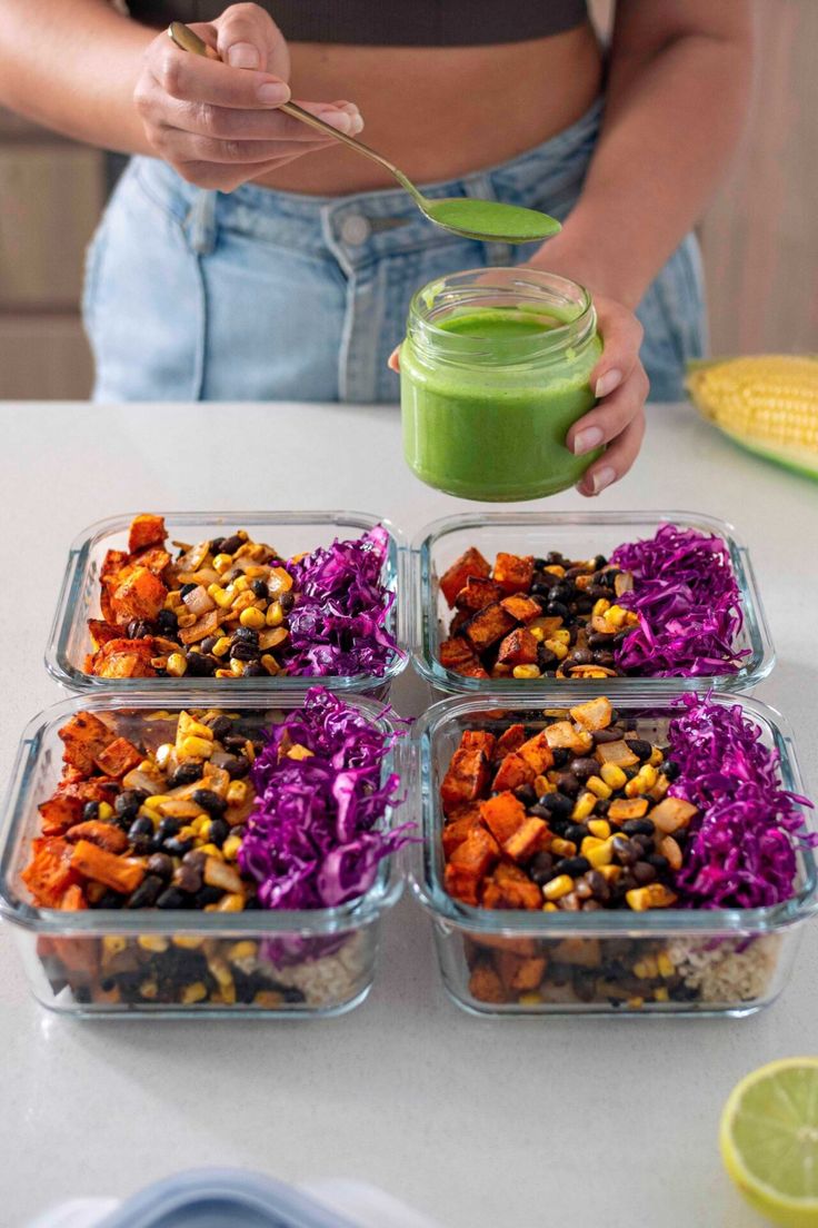 a woman holding a green smoothie over four trays of food