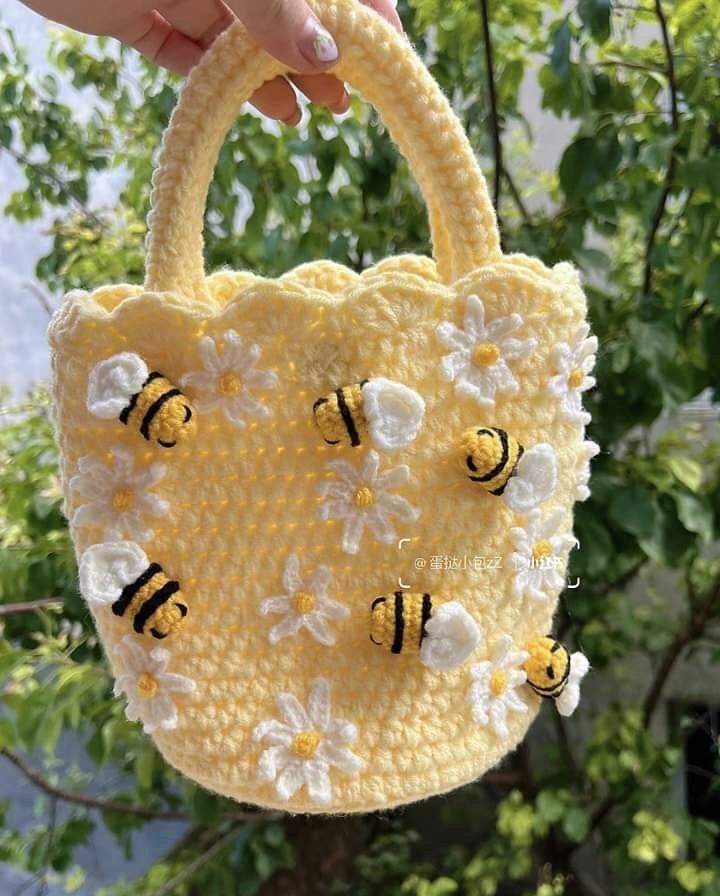 a hand holding a small yellow purse with bees on the front and bottom, while it's made out of yarn