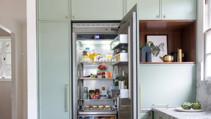 an open refrigerator in a kitchen with green cabinets