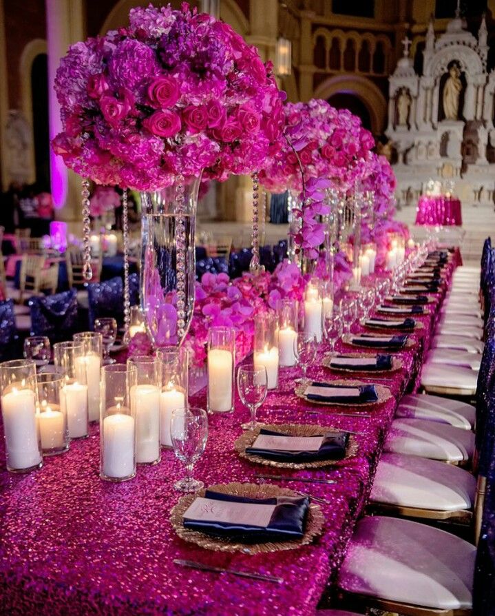 the table is set with candles and pink flowers in tall vases on each side