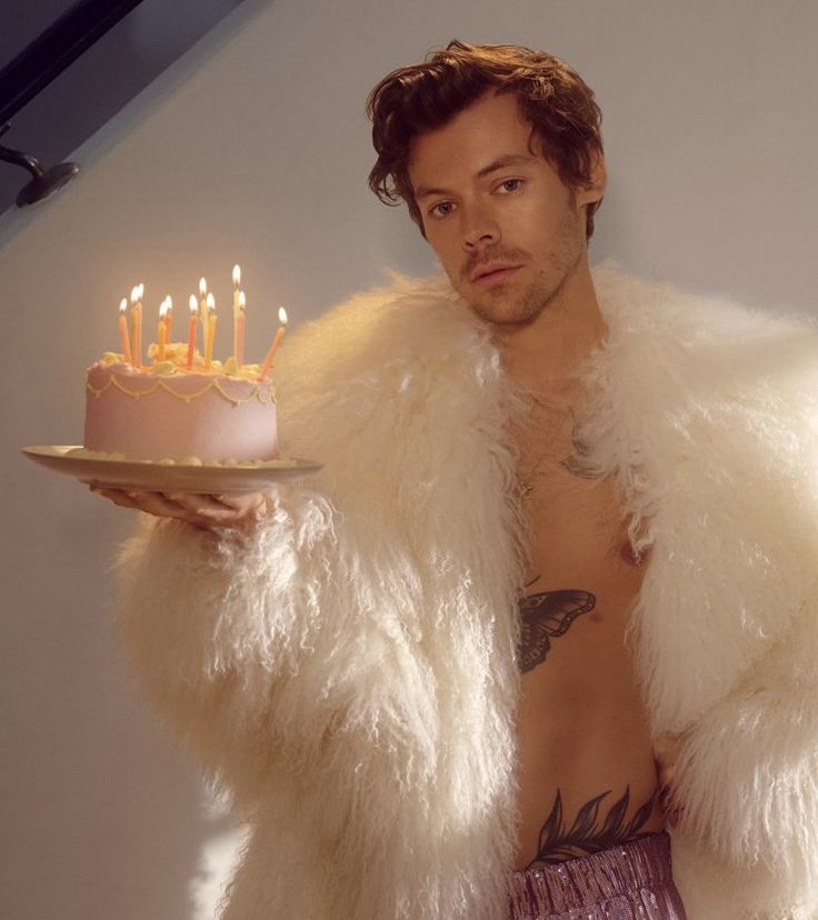 a man holding a cake with candles on it in front of his shirtless body