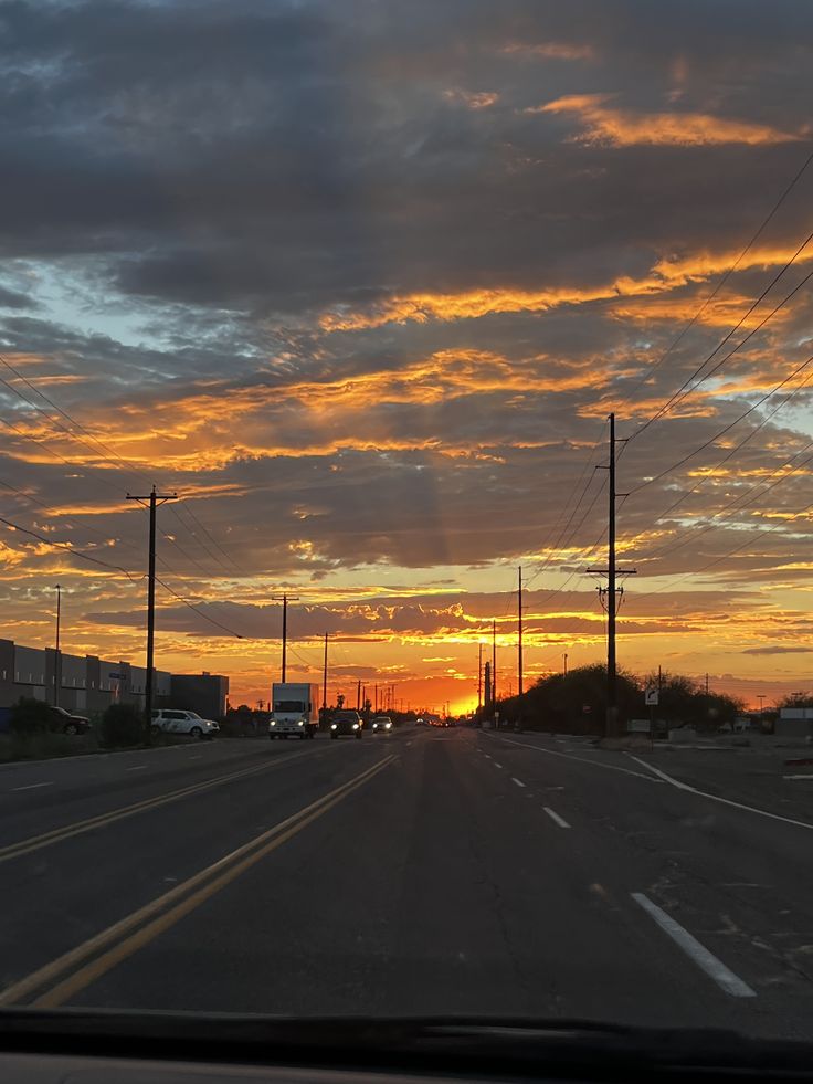 the sun is setting on an empty road with power lines in the distance and cars driving down the street