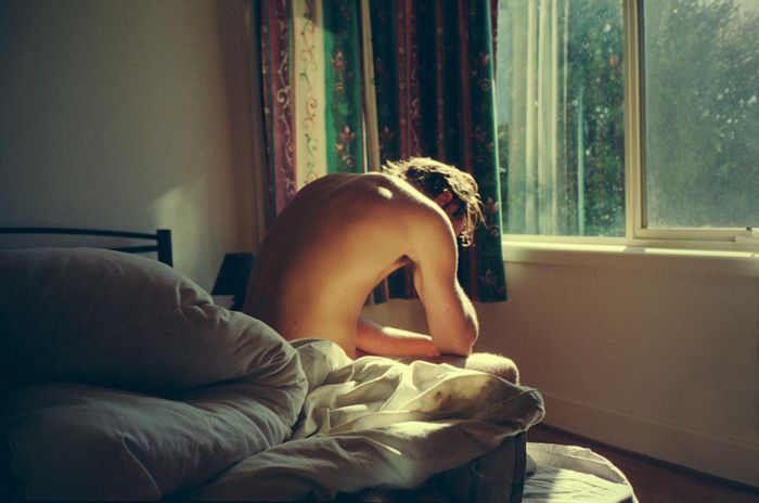 a naked man sitting on top of a bed next to a window