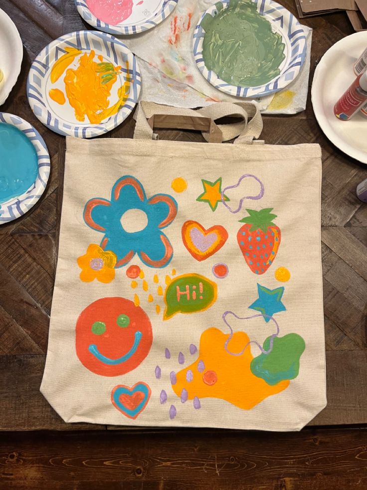 a canvas bag with painted images on it and plates around it, including strawberries