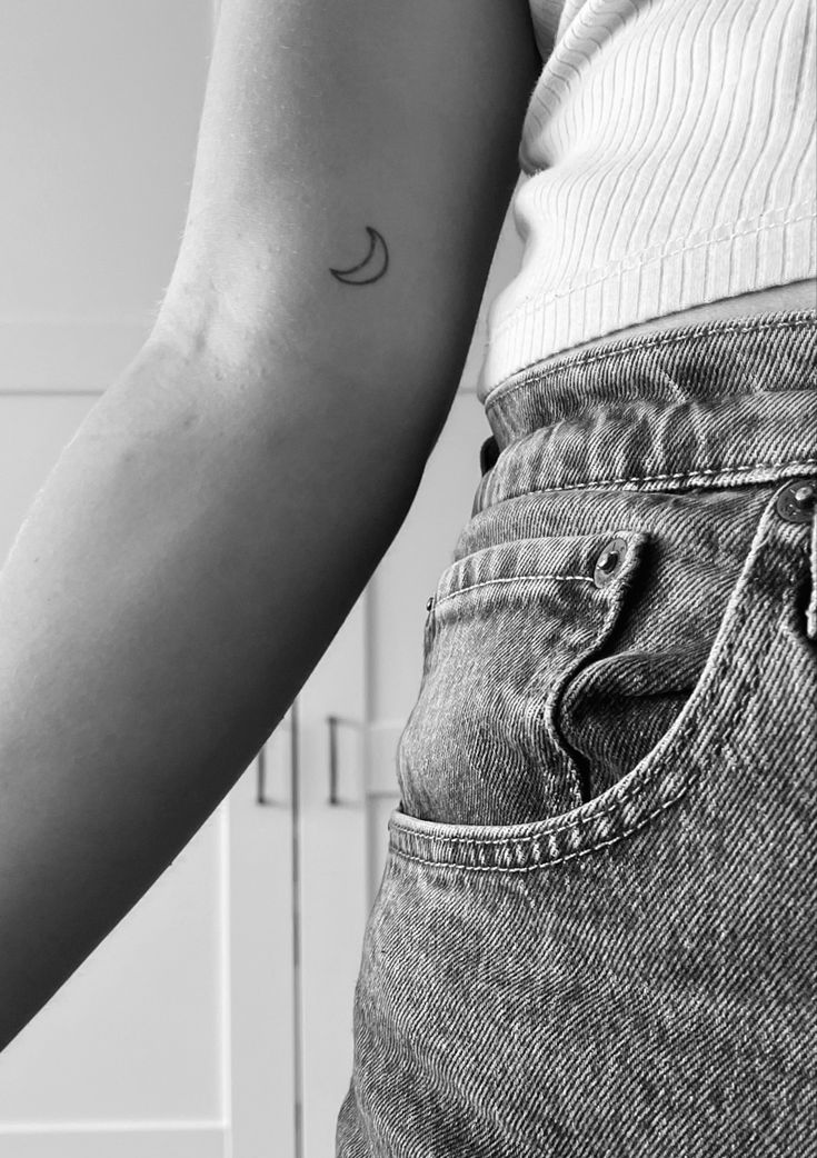 a person with a small crescent tattoo on their arm