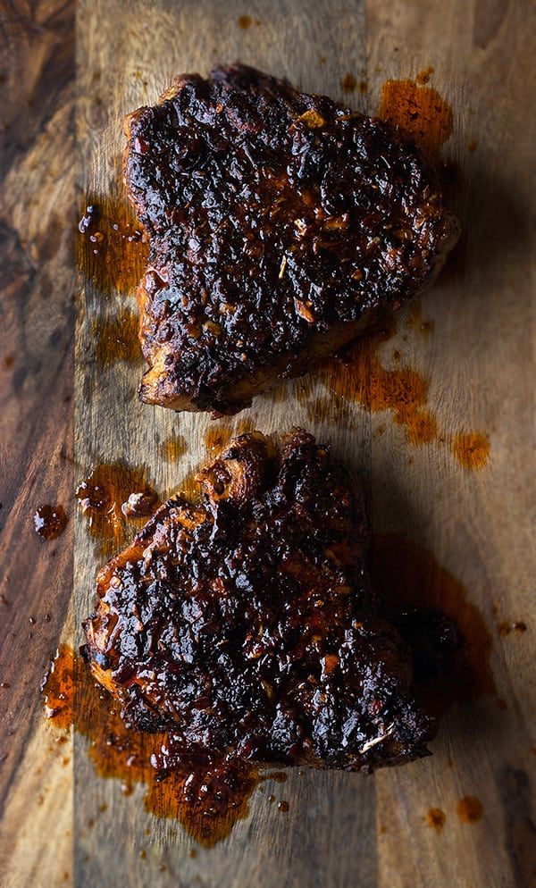 two pieces of meat sitting on top of a cutting board covered in bbq sauce