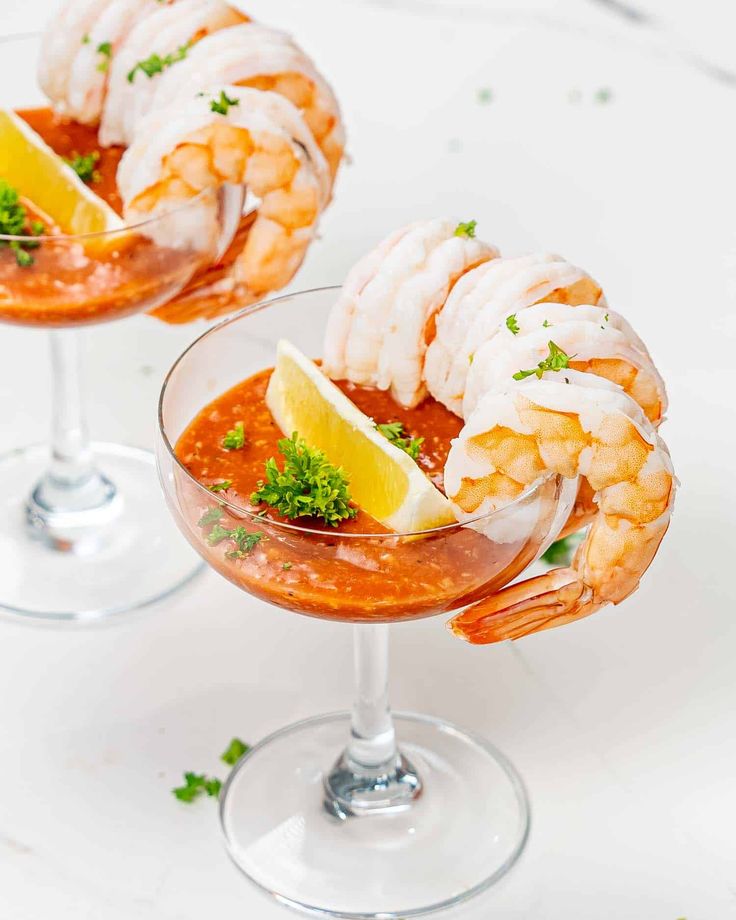 two glasses filled with shrimp and garnish on top of a white countertop